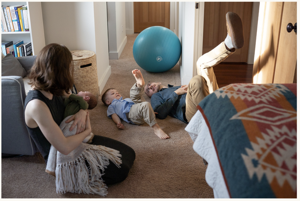 A photo of a new family of four playing together in their bedroom in Shoreline for their in-home newborn session.